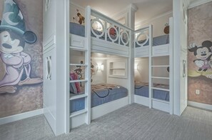 Une chambre d’enfant avec des lits superposés, des tiroirs de rangement et des décorations murales à l’effigie de Mickey Mouse.
