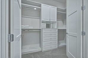 Un dressing accessible sans porte, doté de meubles blancs, d’un ensemble de tiroirs et d’une étagère où sont pliées des serviettes.