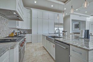 A modern kitchen with white cabinetry, a stainless steel range, and a marble countertop. - Sun-filled Haven With Sports Themed Game Room at Reunion (Kissimmee)