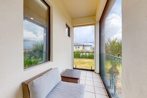 A balcony with a sofa and a small table, a glass door leading outside, and a view of a residential area. - The Epic Portal Mansion (Kissimmee)