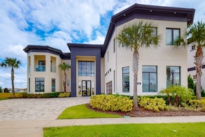 A modern two-story building with a flat roof, large windows, and a well-maintained lawn with palm trees. - The Epic Portal Mansion (Kissimmee)