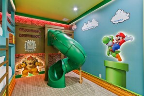 A children's play area with a green slide, a Mario-themed wall, and a brick-patterned wall. - Modern Villa With Games Room at Reunion (Kissimmee)