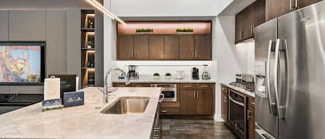 A modern kitchen with a large island, stainless steel appliances, and a flat-screen TV.