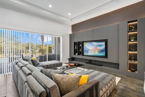 A modern living room with a large flat-screen TV mounted on the wall, a sectional sofa, and a glass coffee table. - Modern Villa With Games Room at Reunion (Kissimmee)