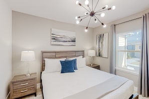 A neatly arranged bedroom with a large bed, bedside tables with lamps, a modern ceiling light fixture, and artwork on the walls. - Magical Sunny Townhouse With Games Room at Reunion (Kissimmee)