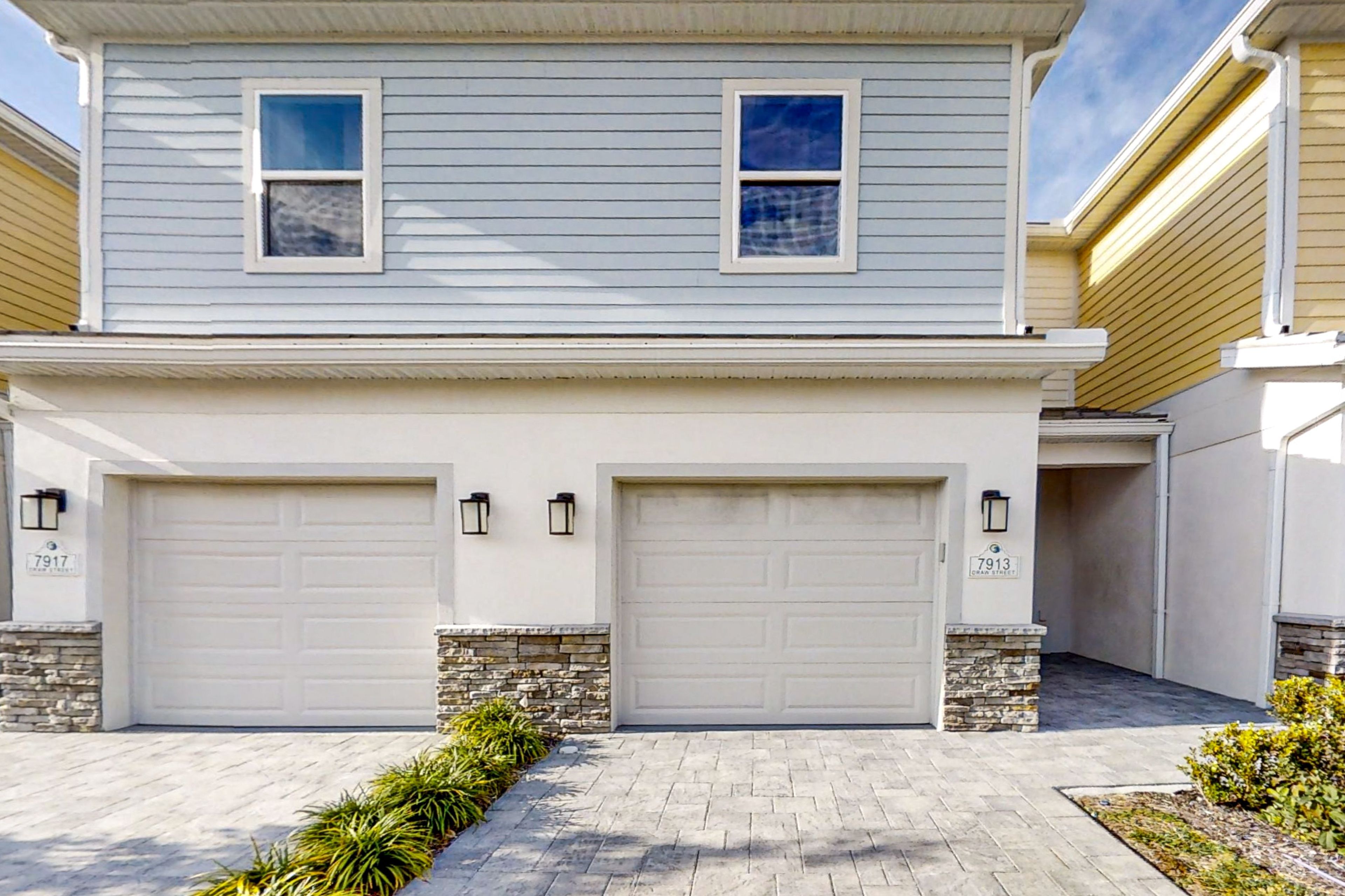 A two-story residential building with two garage doors and a stone foundation.