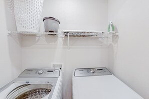 A laundry area with two Samsung washing machines, a white shelf with a basket, and a green bottle. - Magical Sunny Townhouse With Games Room at Reunion (Kissimmee)