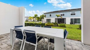 An outdoor patio with a white table and chairs, a clear blue sky, and a residential building in the background. - Getaway Townhome at Reunion Resort (Kissimmee)