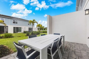 A patio with a white table and chairs, a small garden, and a building in the background. - Getaway Townhome at Reunion Resort (Kissimmee)
