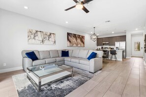 A modern living room with a sectional sofa, a glass coffee table, and artwork on the walls. - Getaway Townhome at Reunion Resort (Kissimmee)