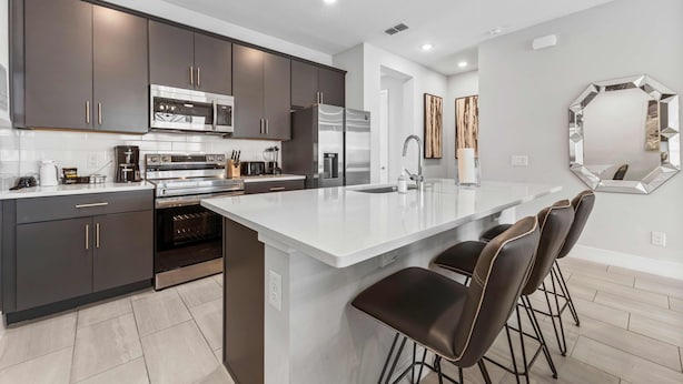 A modern kitchen with dark cabinetry, stainless appliances, and a central island with bar stools. - Getaway Townhome at Reunion Resort (Kissimmee)