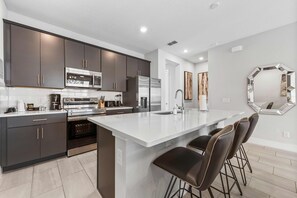 A modern kitchen with dark cabinetry, stainless appliances, and a central island with bar stools. - Getaway Townhome at Reunion Resort (Kissimmee)