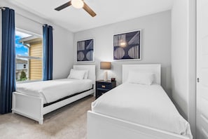 Une chambre avec deux lits simples, une table de chevet avec une lampe et un ventilateur de plafond.