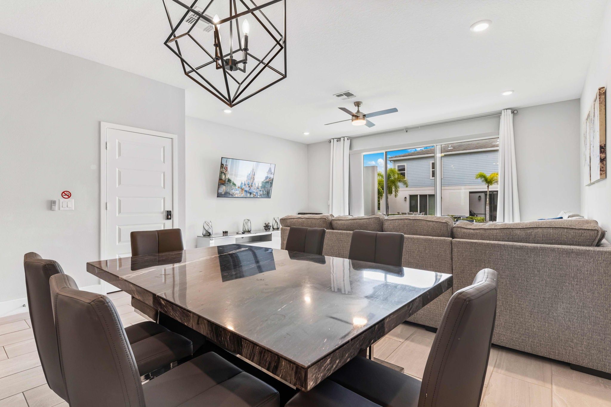 A modern dining area with a large rectangular table and six chairs, a ceiling fan, and a view of the outside.