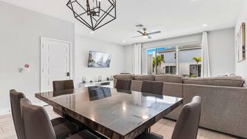 A modern dining area with a large rectangular table and six chairs, a ceiling fan, and a view of the outside.