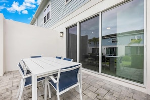 An outdoor patio with a white table and blue chairs, a sliding glass door, and a white wall. - Getaway Townhome at Reunion Resort (Kissimmee)
