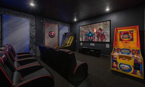 Ein Heimkino mit großem Bildschirm, bequemen Sitzgelegenheiten und einer Krabschmaschine.