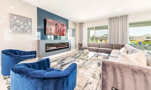 Ein modernes Wohnzimmer mit Flachbildfernseher, blauen und grauen Sofas, einem Couchtisch und einem Kamin.