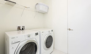 A laundry area with two front-loading washing machines, a white door, and a laundry basket on a wall-mounted rack. - Modern Villa With Fun Themed Bedrooms at Reunion (Kissimmee)