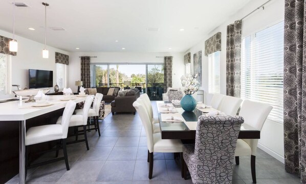 A modern dining area with a long table, white chairs, and a sofa. - Modern Villa With Fun Themed Bedrooms at Reunion (Kissimmee)