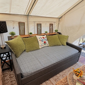A tent with a bed, framed artwork, and a small table with a lamp.
