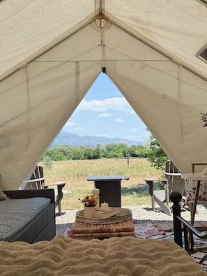 A tent with a view of a field and mountains, a table with candles, and a sofa.