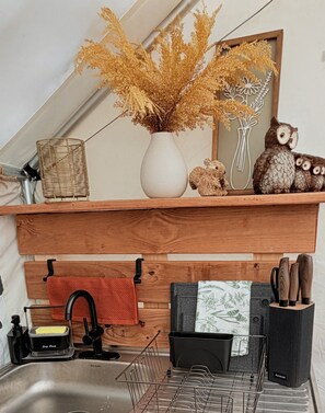 A kitchen with a wooden shelf, a vase with dried plants, a small owl figurine, and a towel hanging on a rack.