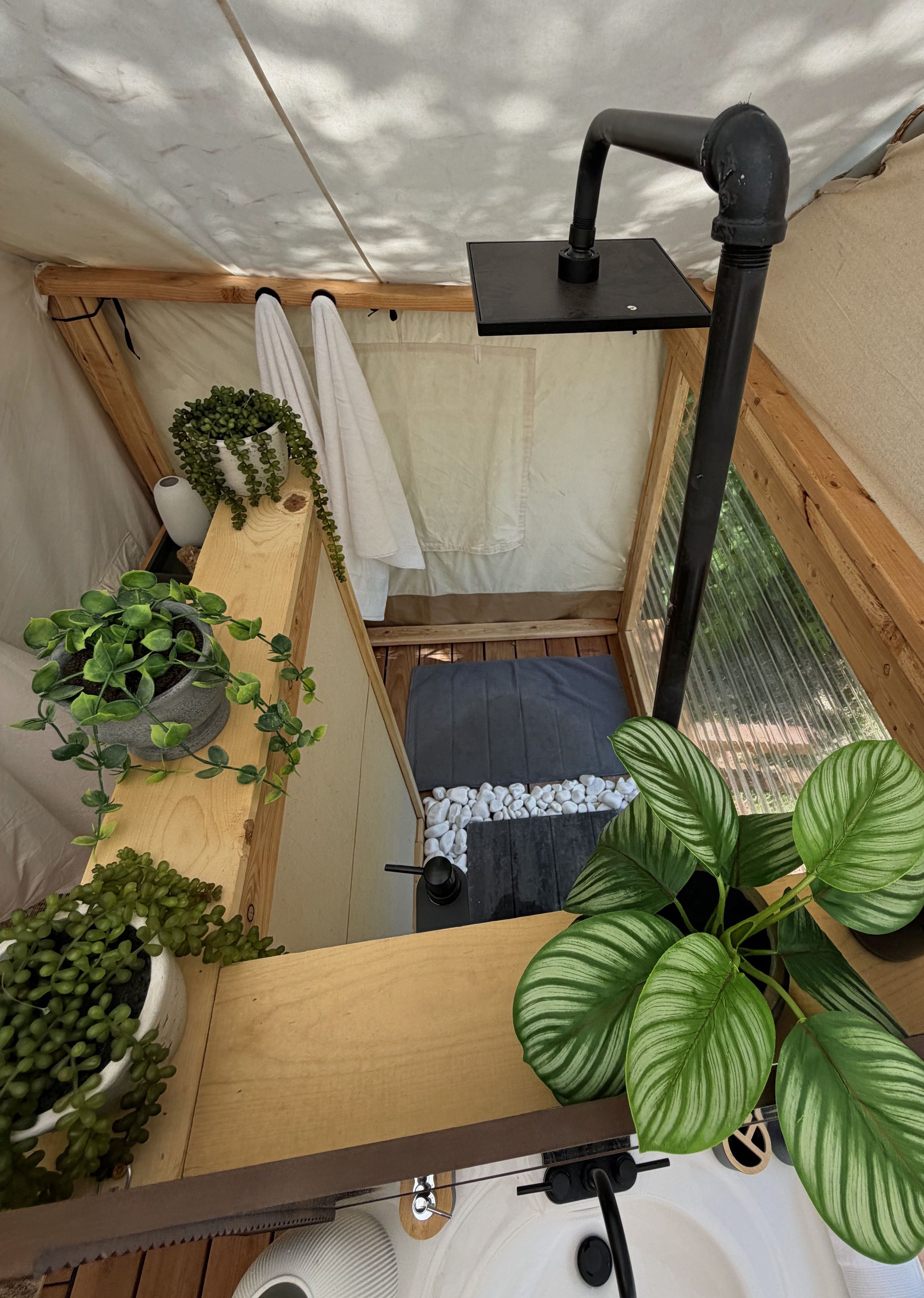 A compact, enclosed space with a bed, a small table, and various potted plants.