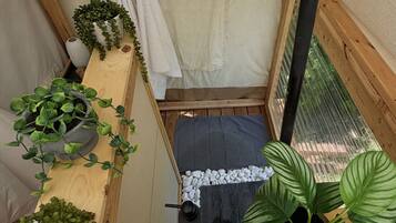 A compact, enclosed space with a bed, a small table, and various potted plants.
