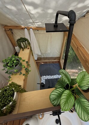 A compact, enclosed space with a bed, a small table, and various potted plants.