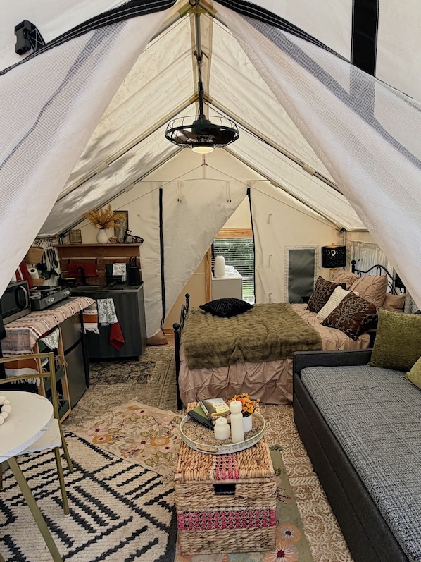 A cozy tented accommodation with a bed, sofa, and a small kitchenette.