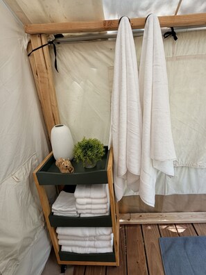 A wooden shelf with folded towels, a small plant, and a decorative item in a tent-like room.