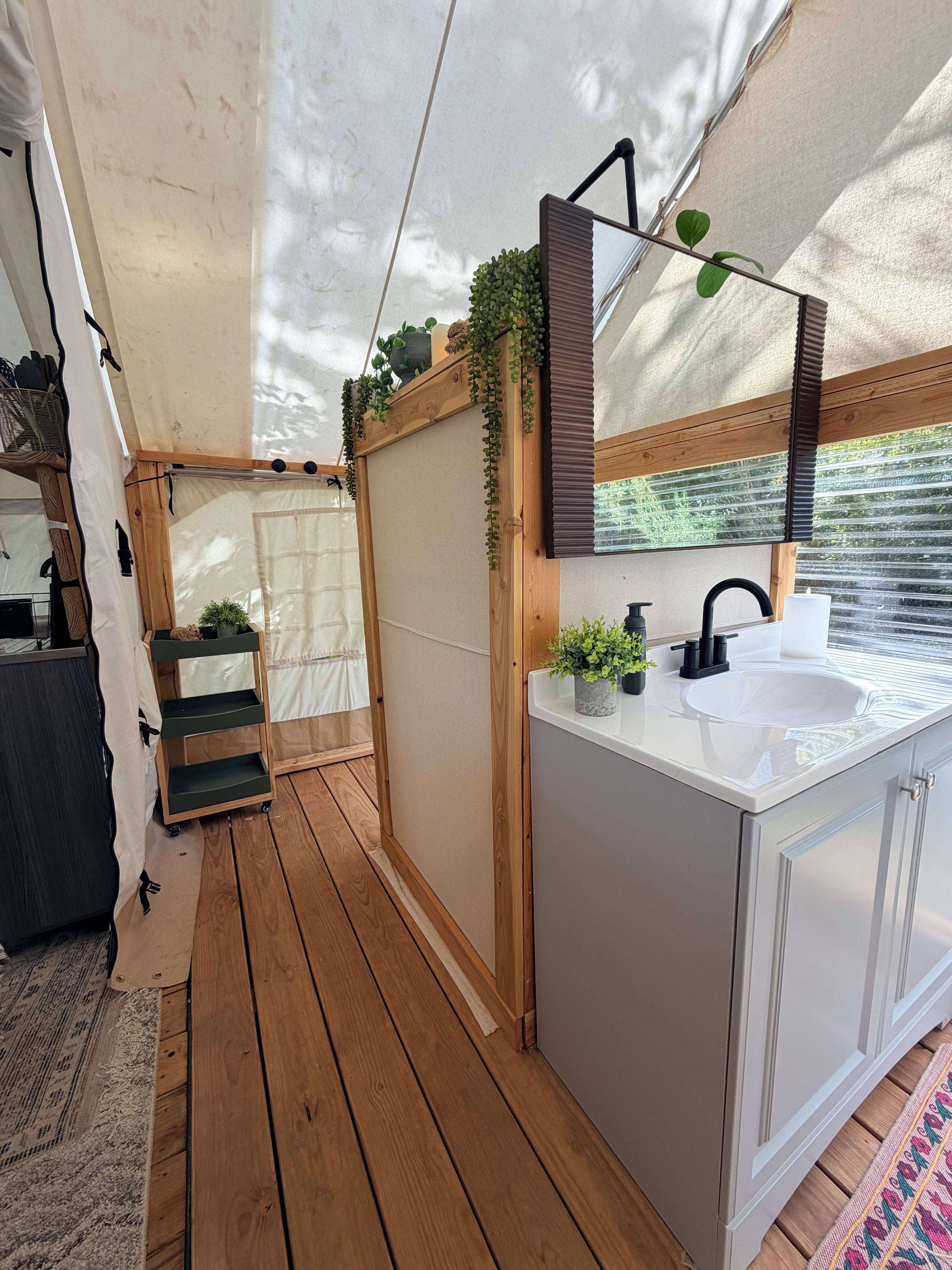 A compact, well-organized bathroom with a wooden floor, a white sink, and a mirror with greenery.