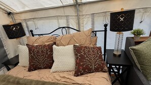 Um quarto com tenda, uma cama, almofadas, uma mesa e um abajur.