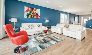 Ein modernes Wohnzimmer mit blauer Akzentwand, weißen Sofas, einem roten Sessel und einem farbenfrohen abstrakten Gemälde.