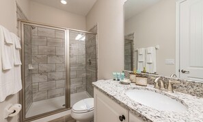 A bathroom with a glass-enclosed shower, a white toilet, a sink with a marble countertop, and a mirror. - Modern Abode With Private Pool and Spa in Encore (Kissimmee)