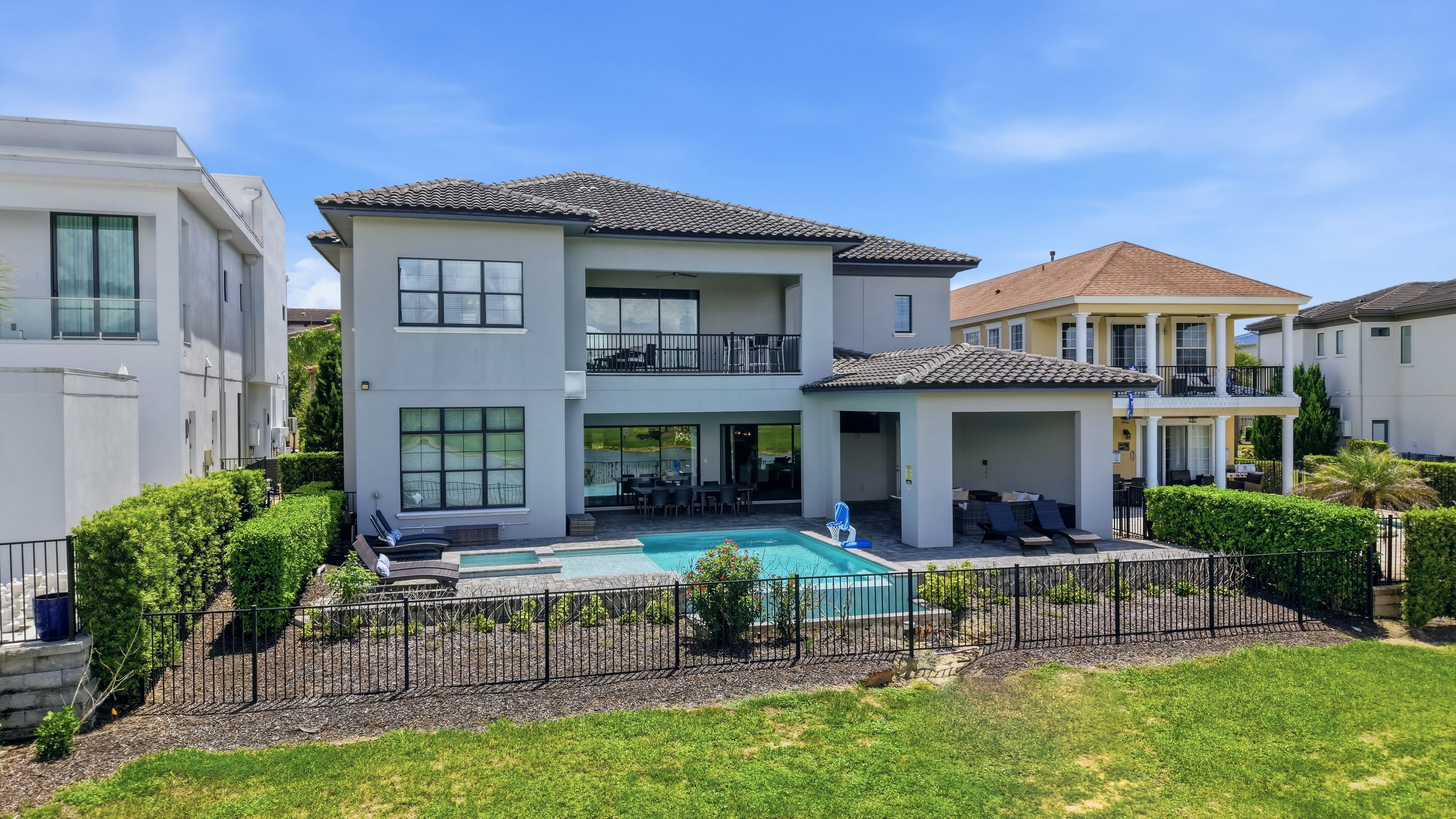 A two-story house with a swimming pool, a covered patio, and a well-maintained lawn.