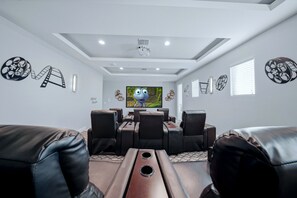 Sala de cinema com uma grande TV de tela plana, poltronas de couro reclináveis e um dispensador de pipoca.