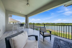 Ein Balkon mit Blick auf einen See und Häuser, ausgestattet mit einer Couch und Stühlen.