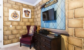 A room with a stone wall, a red armchair, a TV mounted on the wall, and a sign that reads "Hogwarts". - Sleek Home With Stunning Game Room at Reunion (Kissimmee)