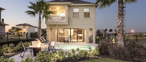 A two-story house with a swimming pool, outdoor seating, and palm trees.
