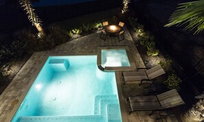 A rectangular swimming pool with a hot tub, surrounded by a brick patio. There are lounge chairs and a table with chairs. - Sleek Home With Stunning Game Room at Reunion (Kissimmee)