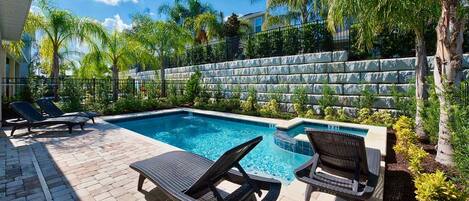 A rectangular swimming pool with two lounge chairs and a small deck area.