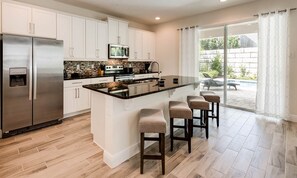 A modern kitchen with white cabinets, a stainless steel refrigerator, a microwave, and a gas stove. There is a large island with bar stools. - Encore Villa With Pool, 10 min to Disney (Kissimmee)