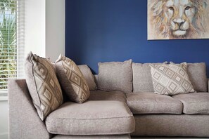A grey sofa with patterned cushions, a blue accent wall, and a painting of a lion's face. - Chic 4BR Contractor Stay for 7+WiFi | Stay With Us (Stockton-on-Tees)