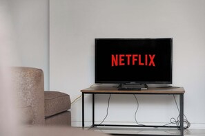 A television on a stand with the word 'NETFLIX' displayed on the screen. - Chic 4BR Contractor Stay for 7+WiFi | Stay With Us (Stockton-on-Tees)