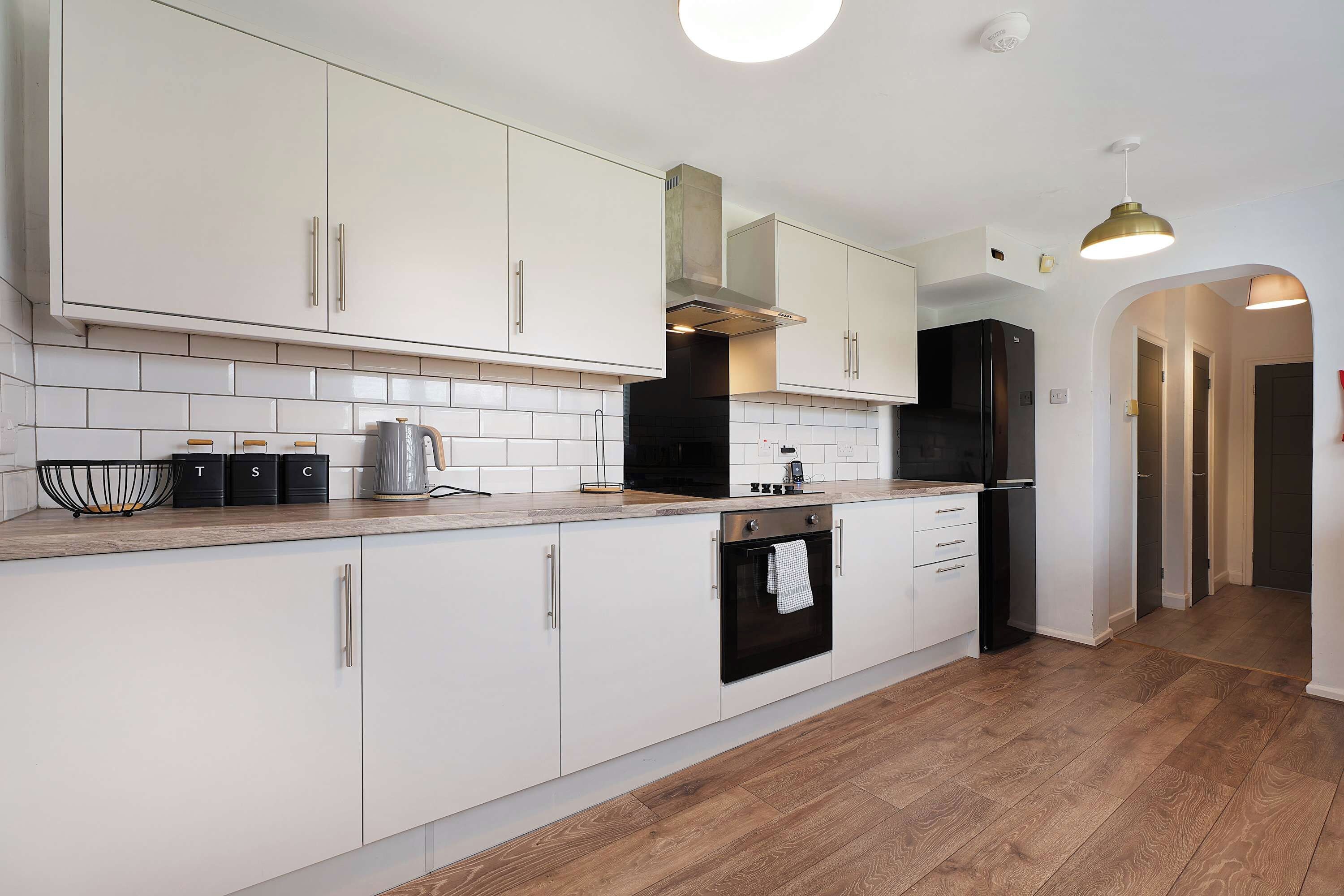 Une cuisine moderne avec des meubles blancs, un réfrigérateur noir et un plan de travail en bois.