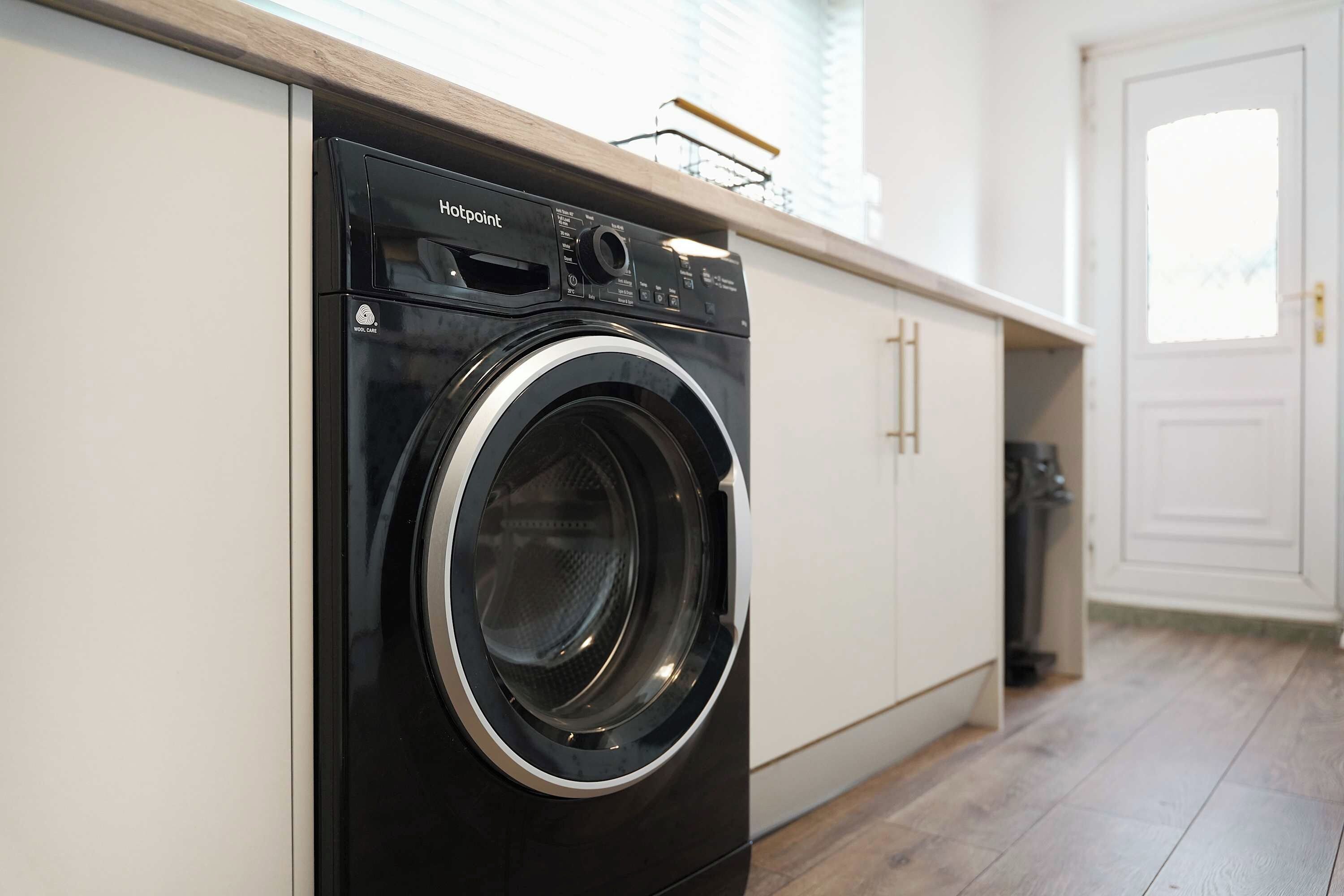 A modern, compact washing machine in a clean, minimalist kitchen with white cabinetry and a wooden countertop.