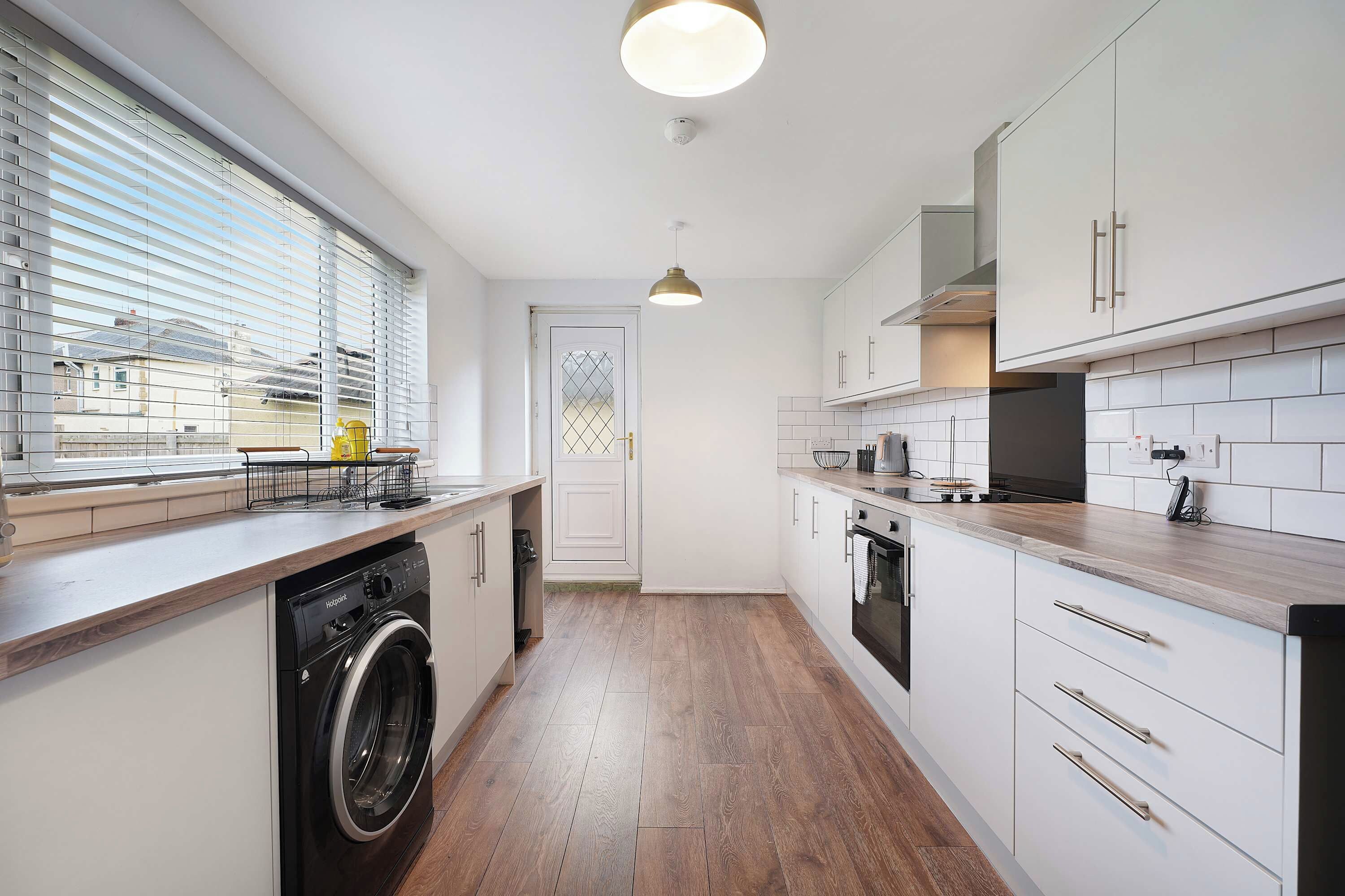 Una cucina moderna con lavatrice integrata, un'ampia finestra con tende e vista esterna.