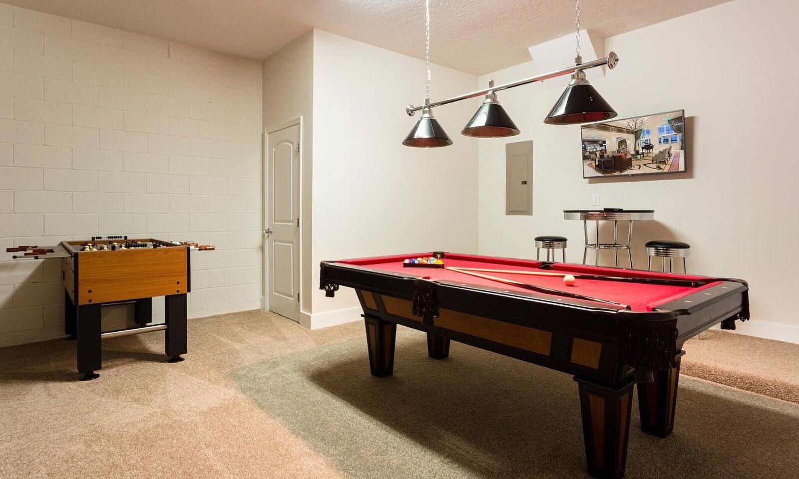 Una habitación con mesa de billar, mesa de fútbolín y una zona de bar con taburetes.